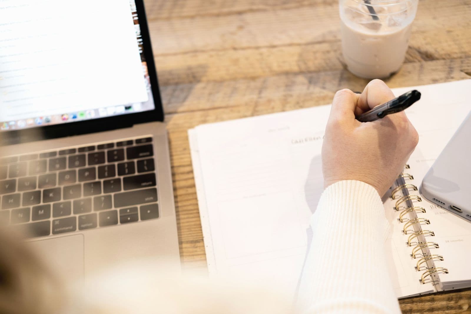 Hand writing notes in a notebook next to a laptop